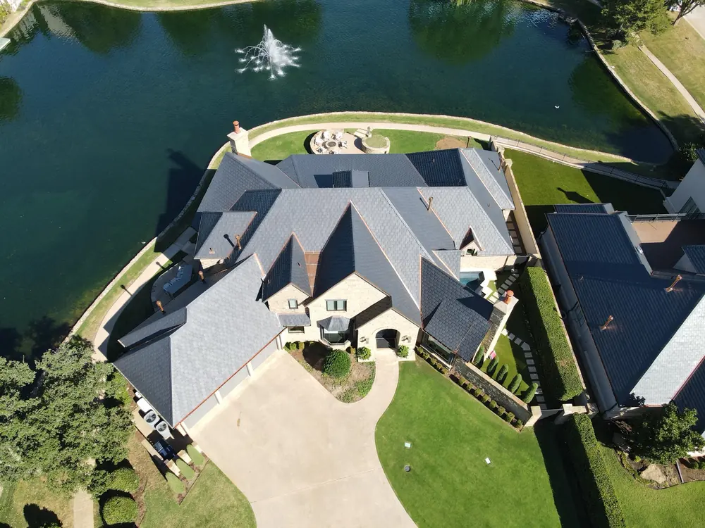 Overhead aerial of a lakefront stone home with an EcoStar synthetic slate roof and copper accents