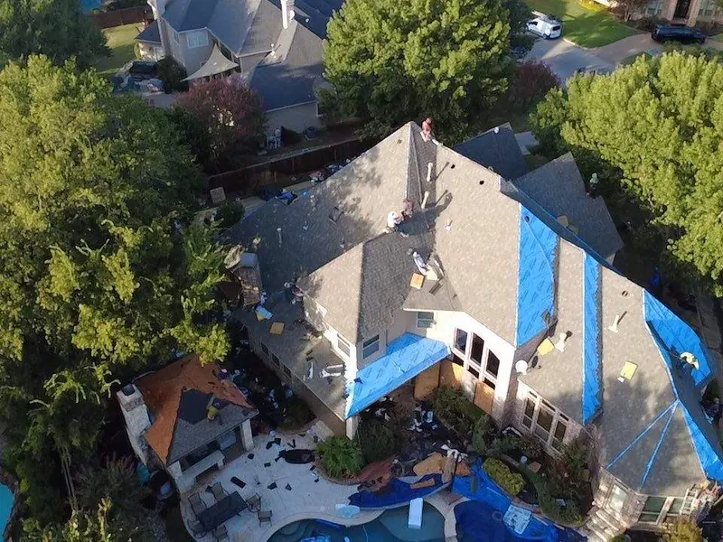Aerial of a storm-damaged roof with blue tarps during tear-off
